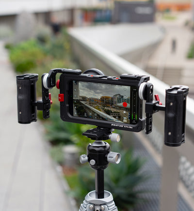 Lifestyle shot of Beastcage for iPhone 16 Pro or 16 Pro Max with RT and LT Mounts facing rear, dual Beastgrip side handles, and 0.75X wide-angle lens — mounted on tripod via Beastgrip Quick Release Plate and filming with Beastcam app for cinematic mobile content creation.